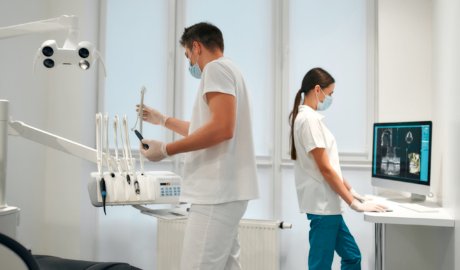 Young dentist prepares tools for work while assistant examines x-ray on a computer. Dentistry and dental care.